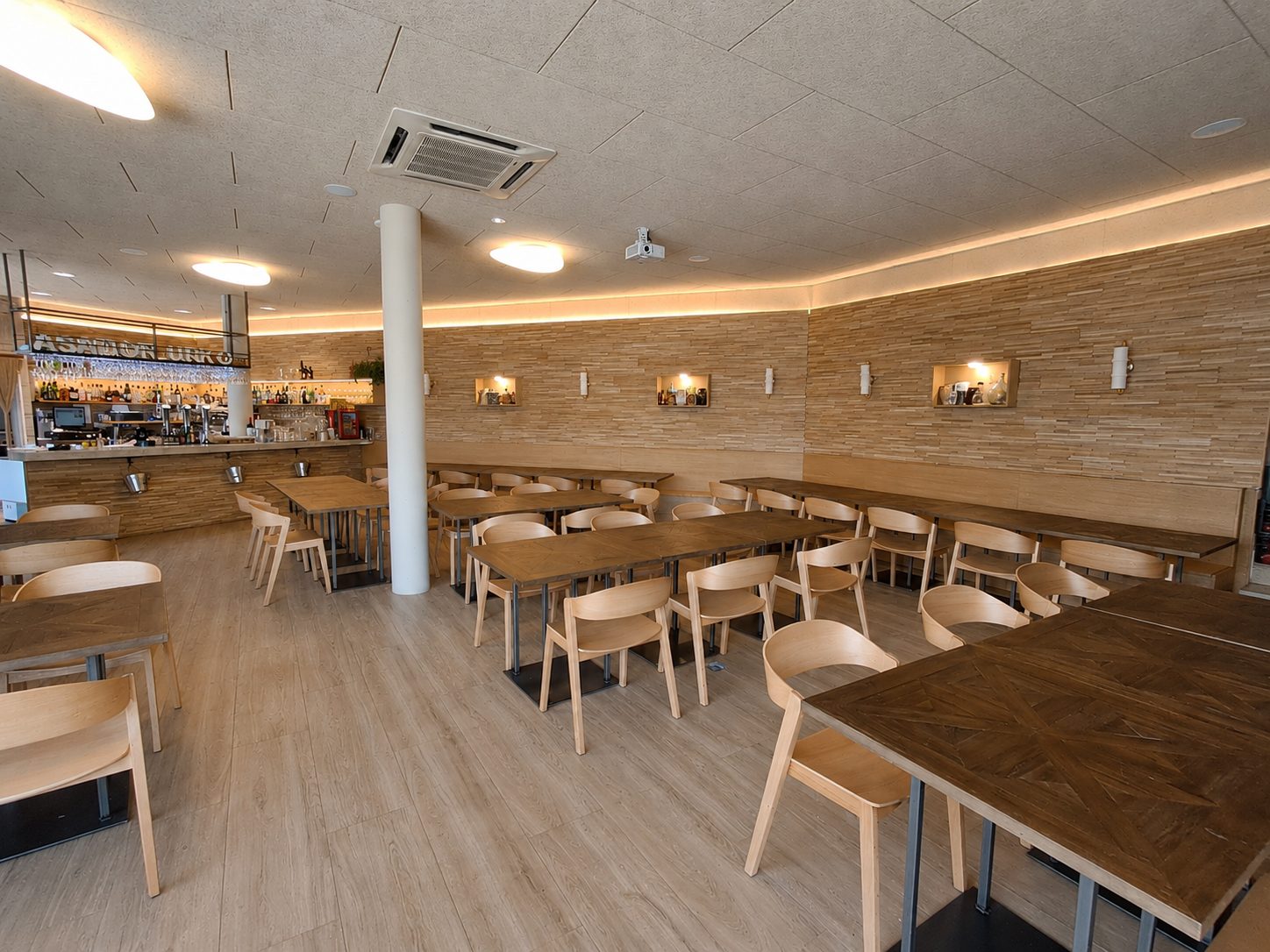 Comedor principal de Urko Bar Asador con mesas de madera alargadas, sillas claras y la barra del asador al fondo
