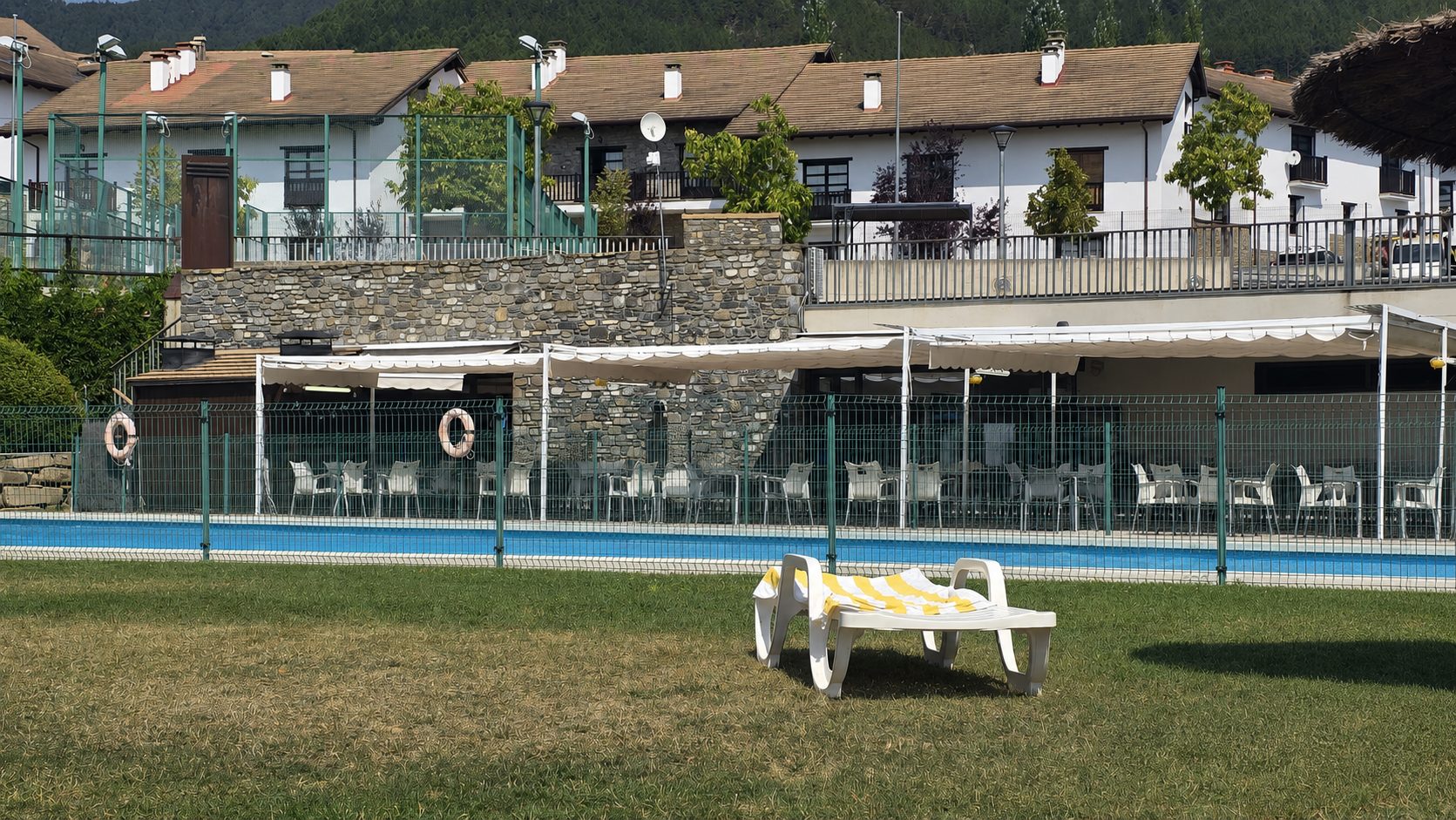 Terraza exterior de Urko Bar Asador con mesas bajo toldos blancos, piscina y montaña al fondo, en Badaguás (Jaca)